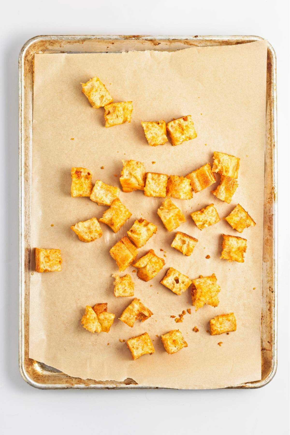Bread cubes spread on a lined baking sheet ready to be baked into croutons.