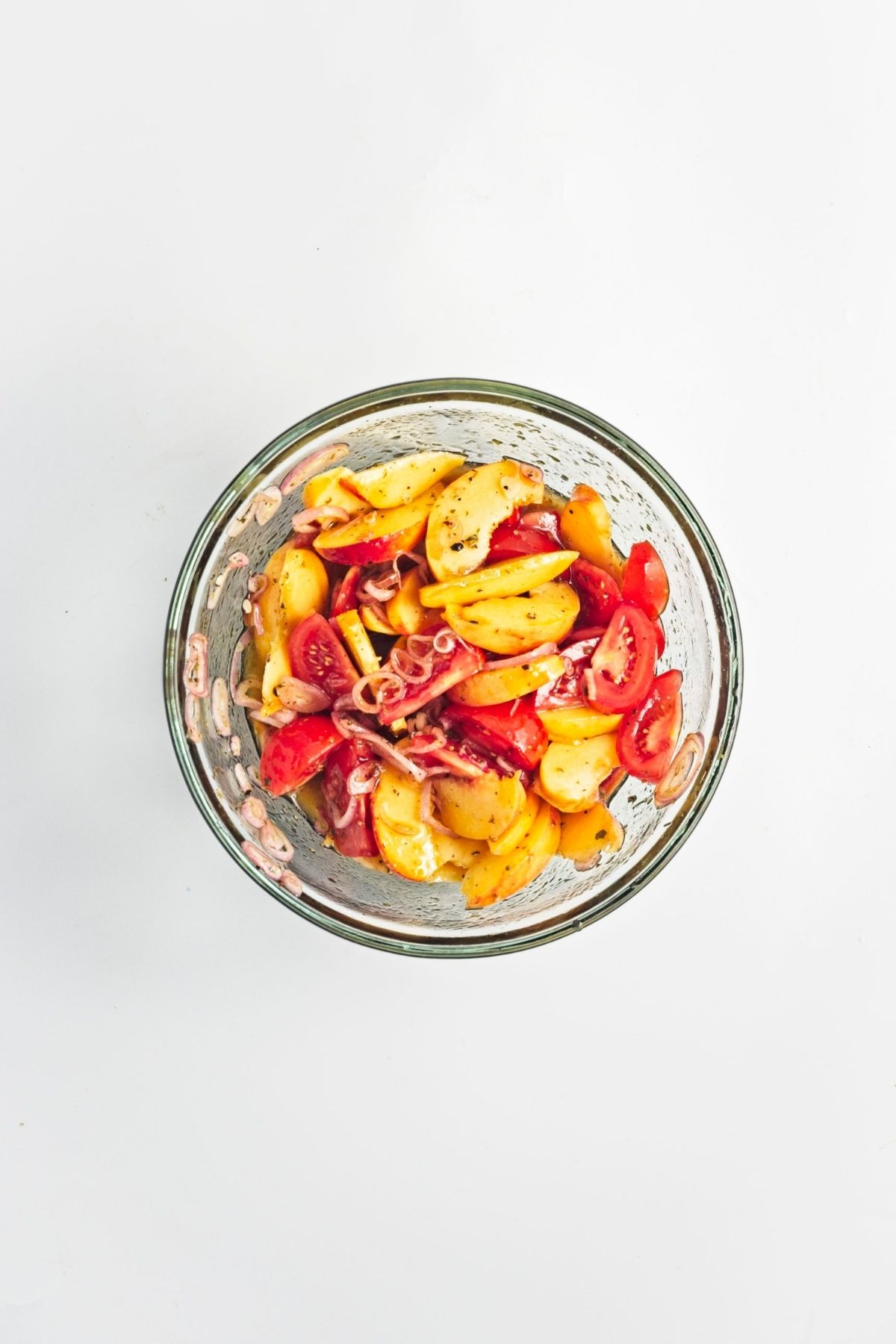 Peach and tomato mixture combined with dressing in a glass bowl before assembling the salad.