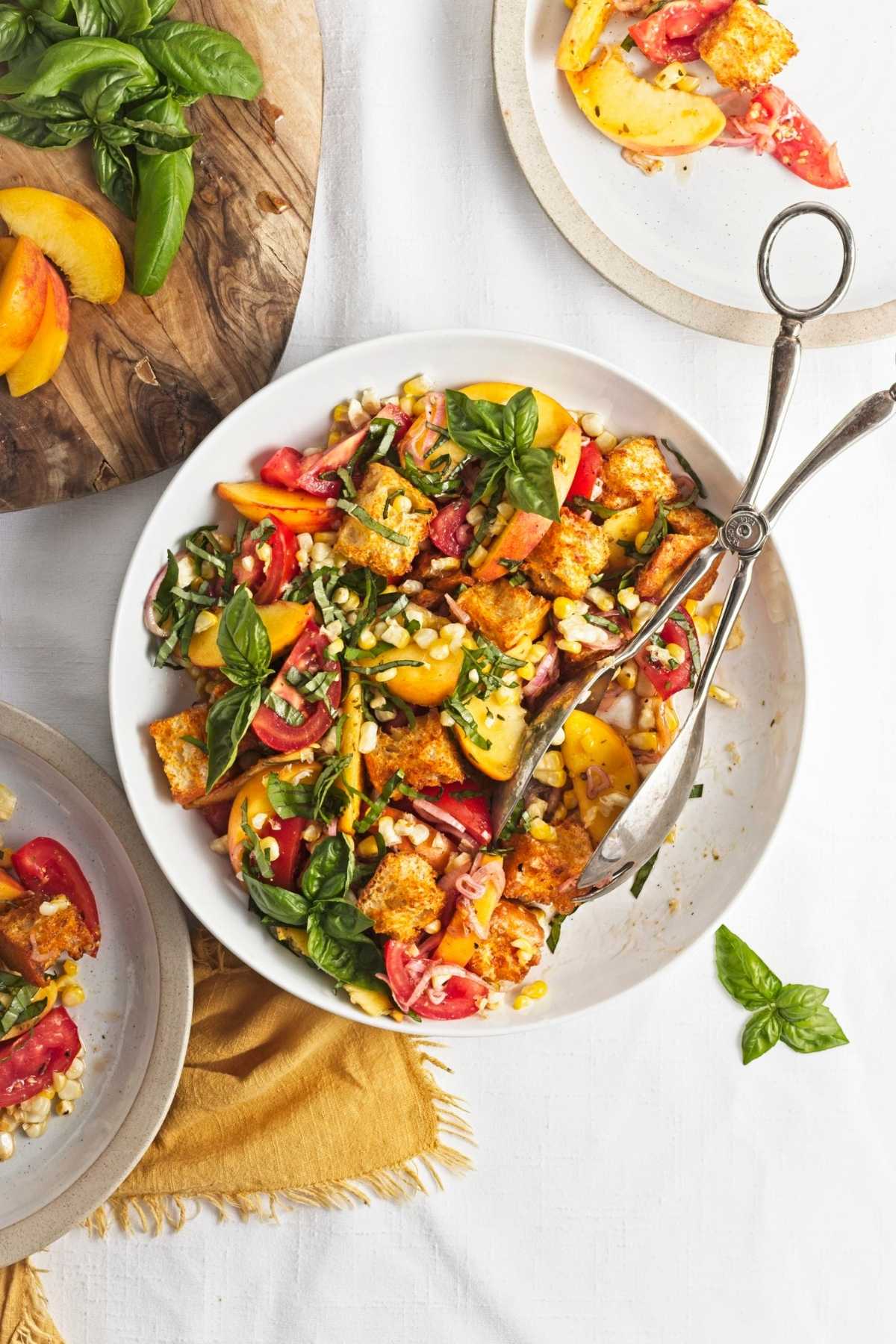Peach and corn panzella salad with roasted corn, ripe peaches, tomatoes, basil, and crispy croutons in a white serving bowl.