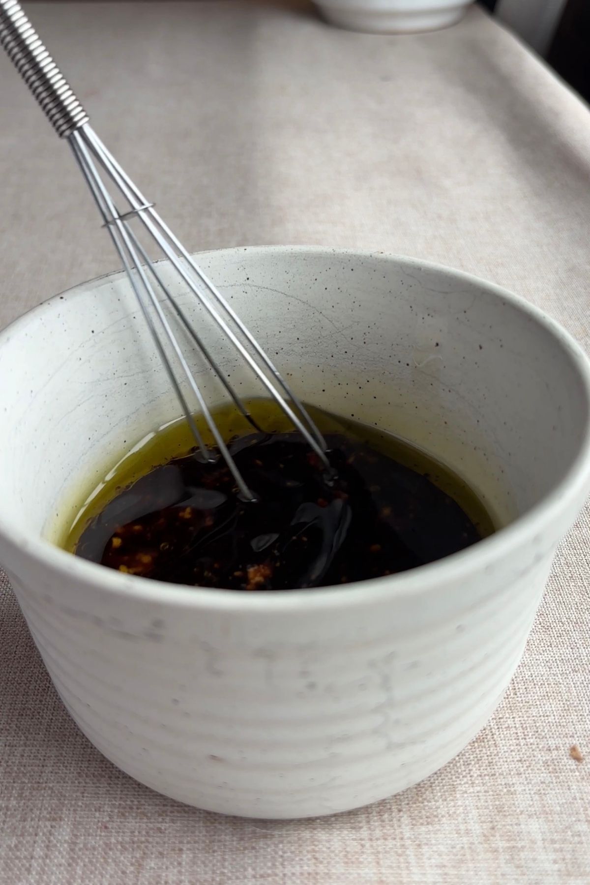 Balsamic dressing ingredients whisked together in a small ceramic bowl with visible olive oil and vinegar.