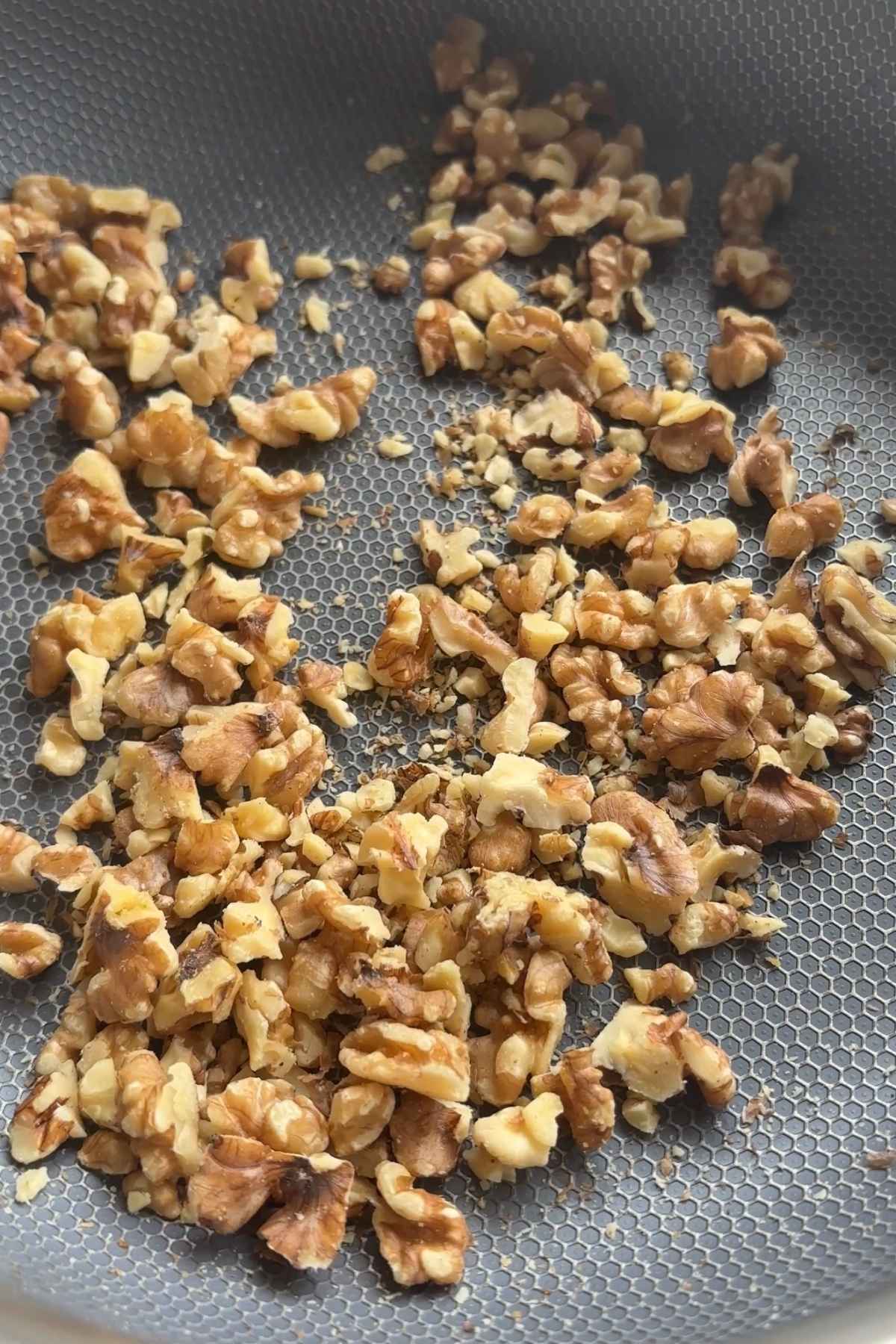Chopped walnuts spread across a dry nonstick skillet, shown before or during toasting.