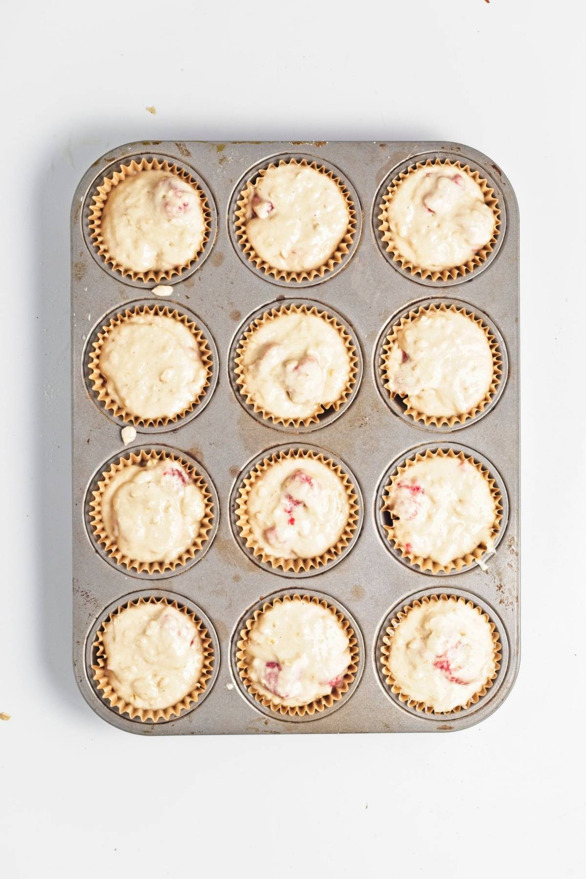 Raspberry oat muffin batter spooned evenly into lined muffin tin wells.