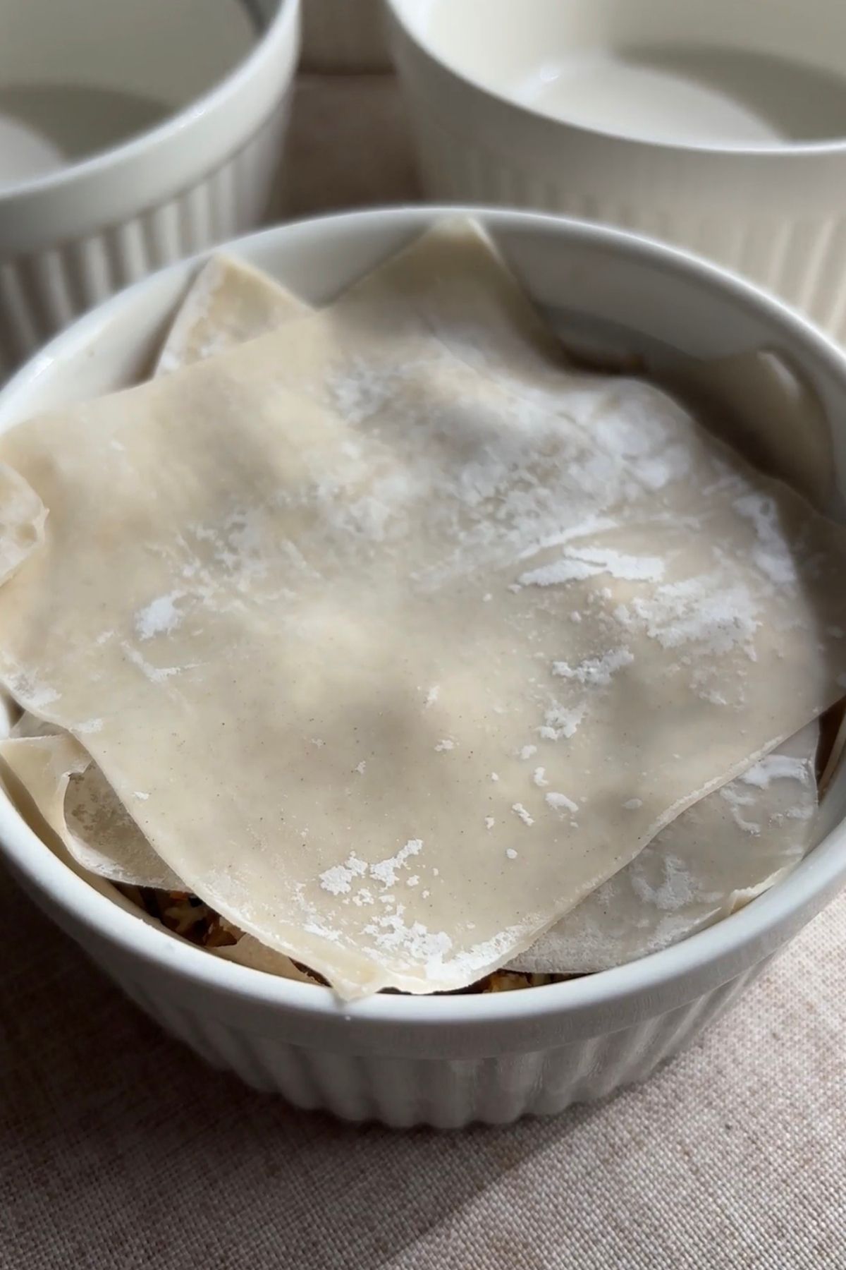 Wonton wrappers layered over dumpling filling inside a white ramekin before adding broth.
