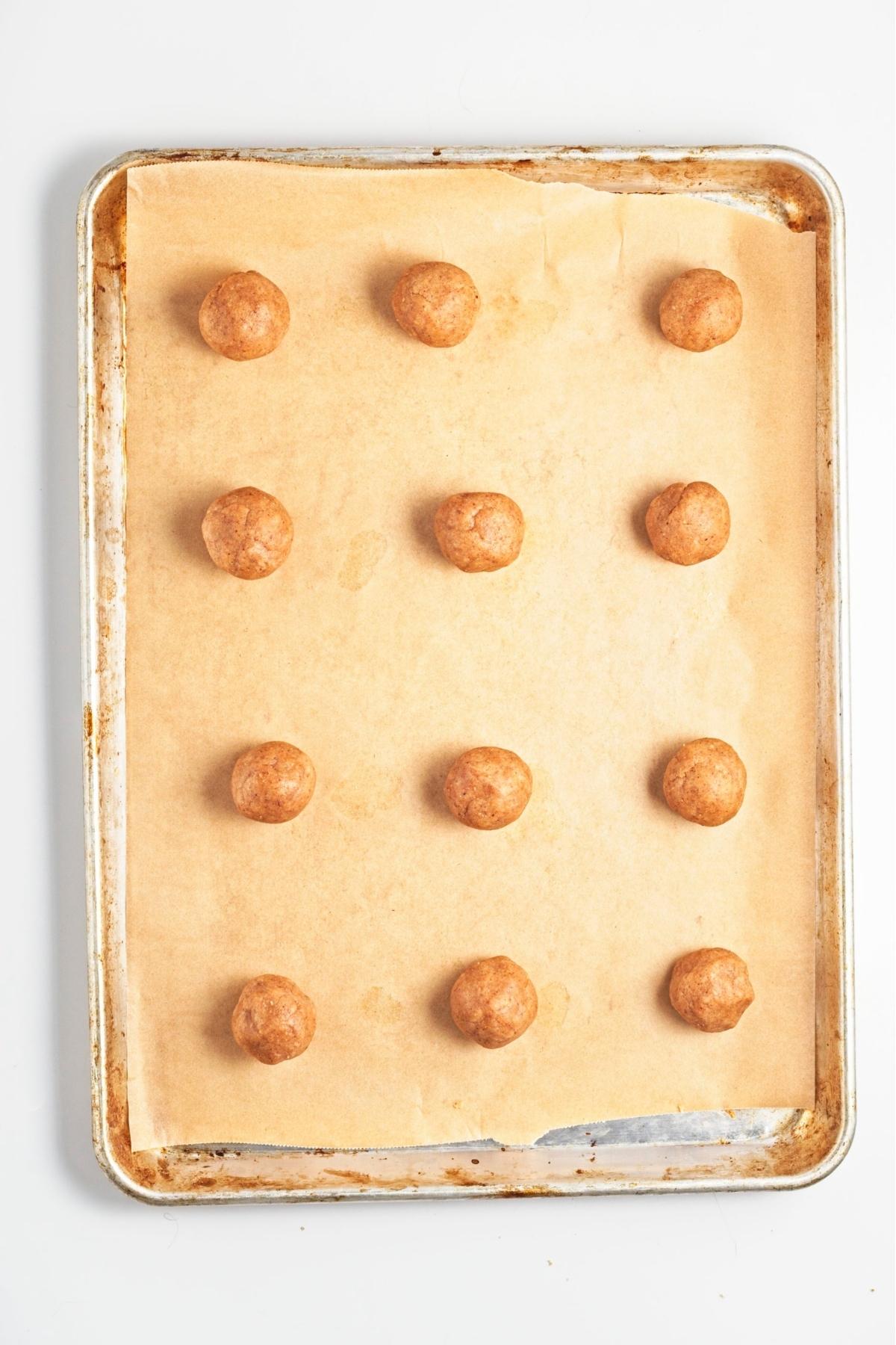 Rolled almond cookie dough balls arranged on a lined baking tray