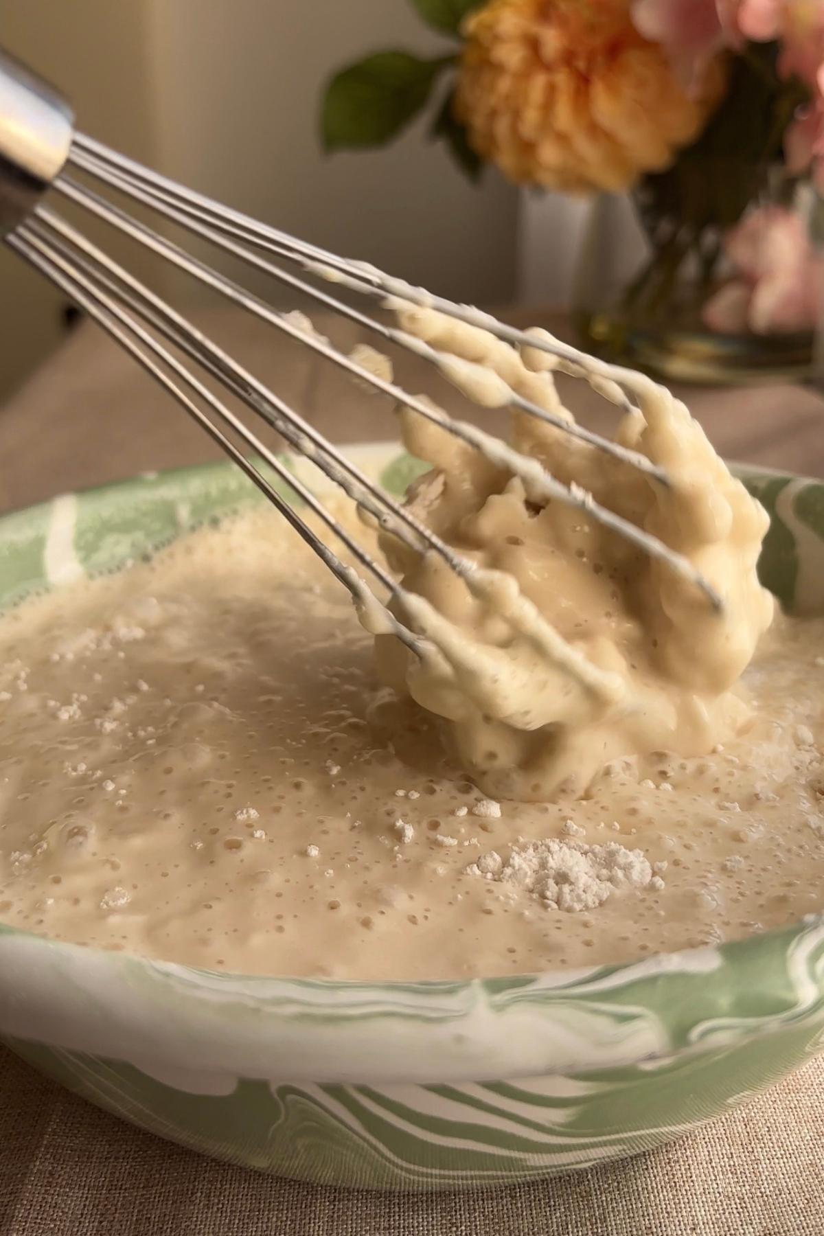 Thick pancake batter clinging to a whisk as itโs lifted from the bowl.