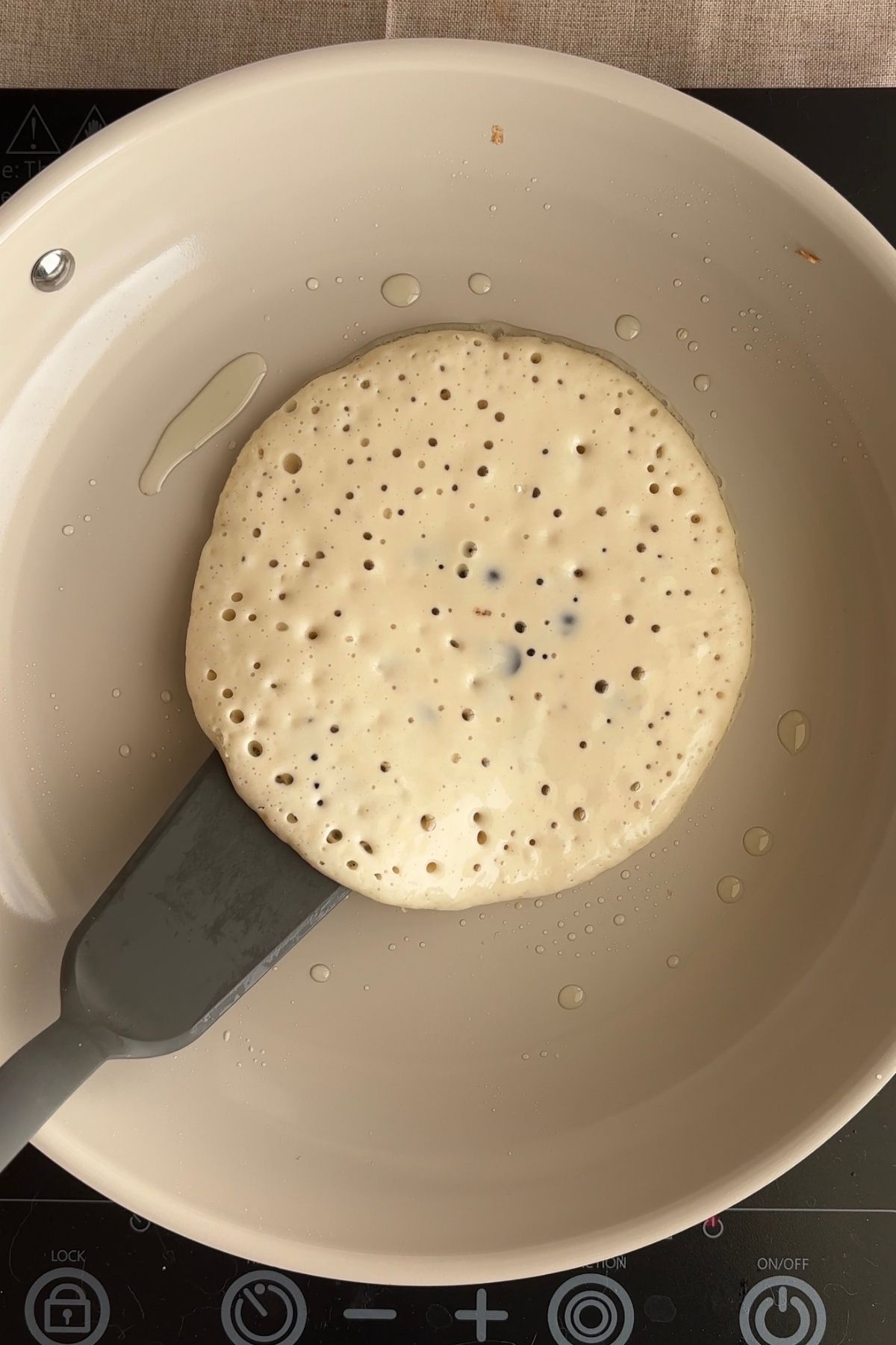 Pancake batter cooking in a skillet with bubbles forming on the surface.