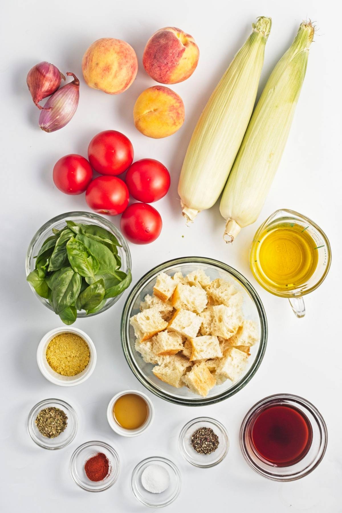 Ingredients for peach and corn panzella including fresh corn, peaches, tomatoes, basil, bread cubes, olive oil, vinegar, shallots, and seasonings.