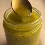 Spoon lifting lemon Dijon dressing from an open glass jar, showing its lightly emulsified texture.