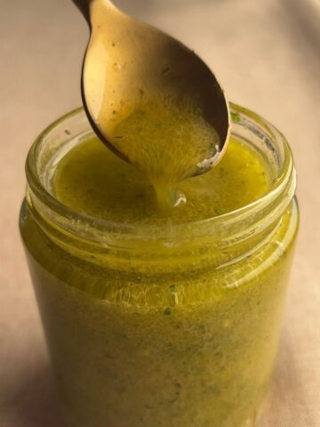 Spoon lifting lemon Dijon dressing from an open glass jar, showing its lightly emulsified texture.