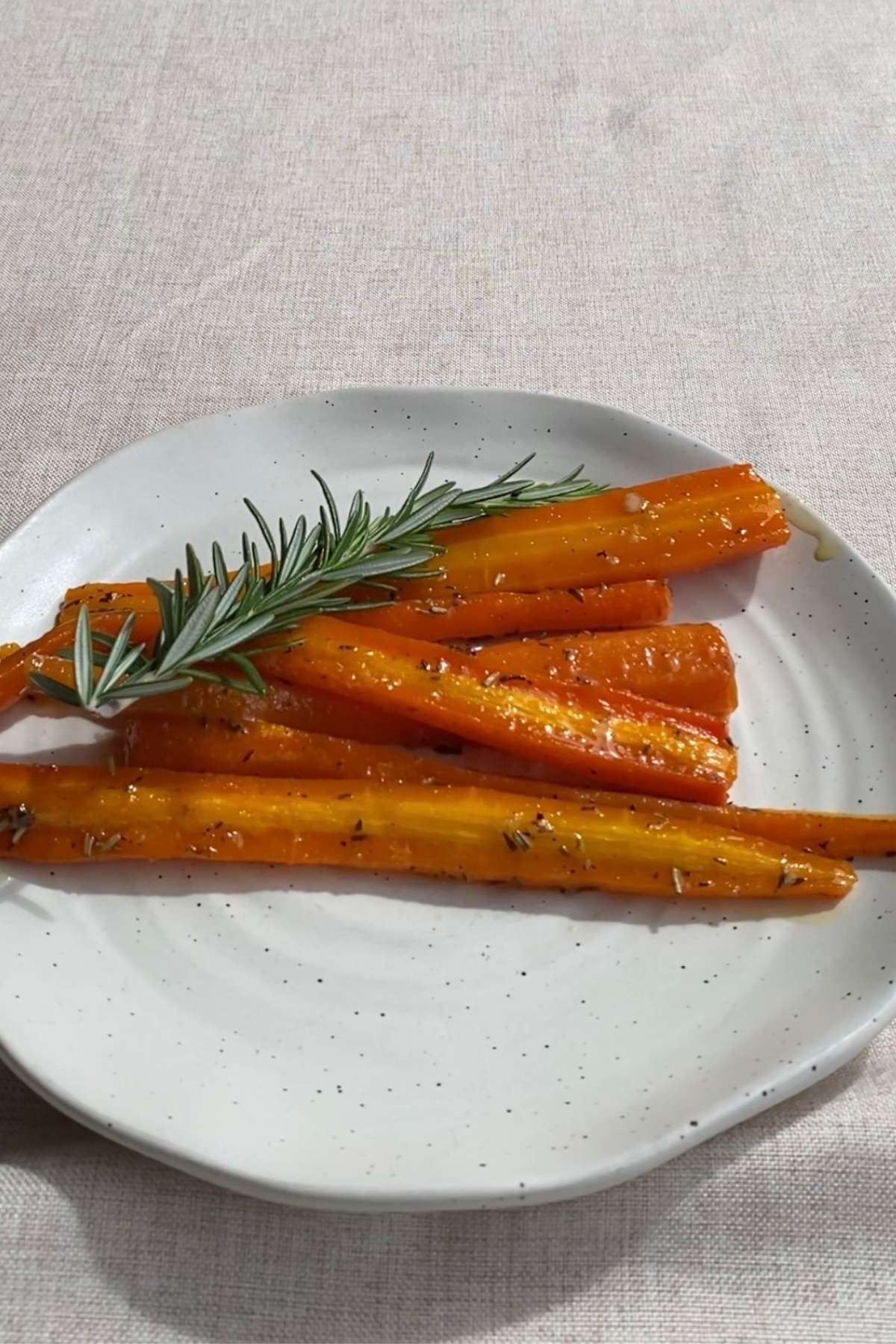 Roasted carrots coated in a shiny glaze, garnished with a rosemary sprig on a ceramic plate.