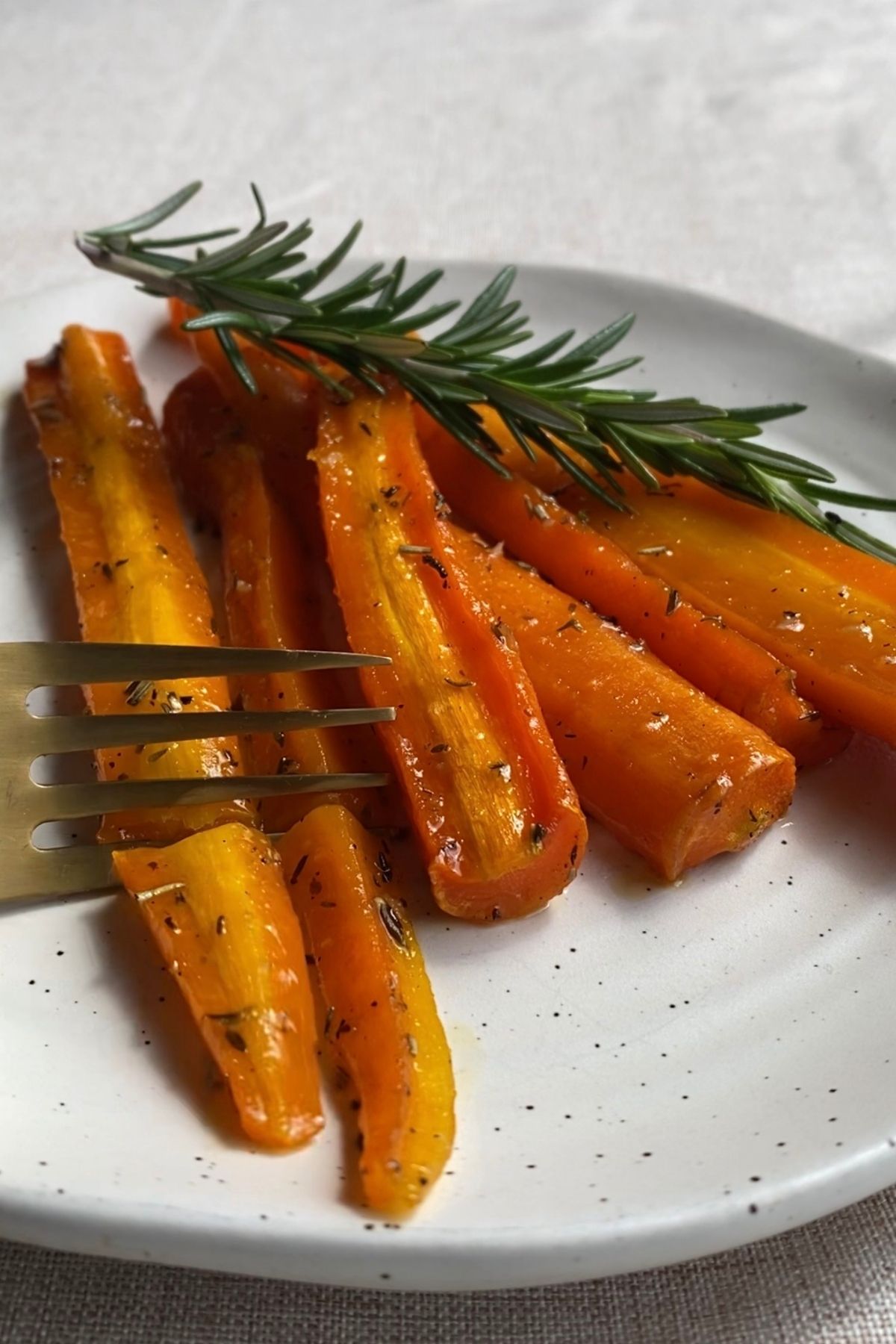 Fork cutting a tender glazed carrot from a plate, showing the caramelized surface.