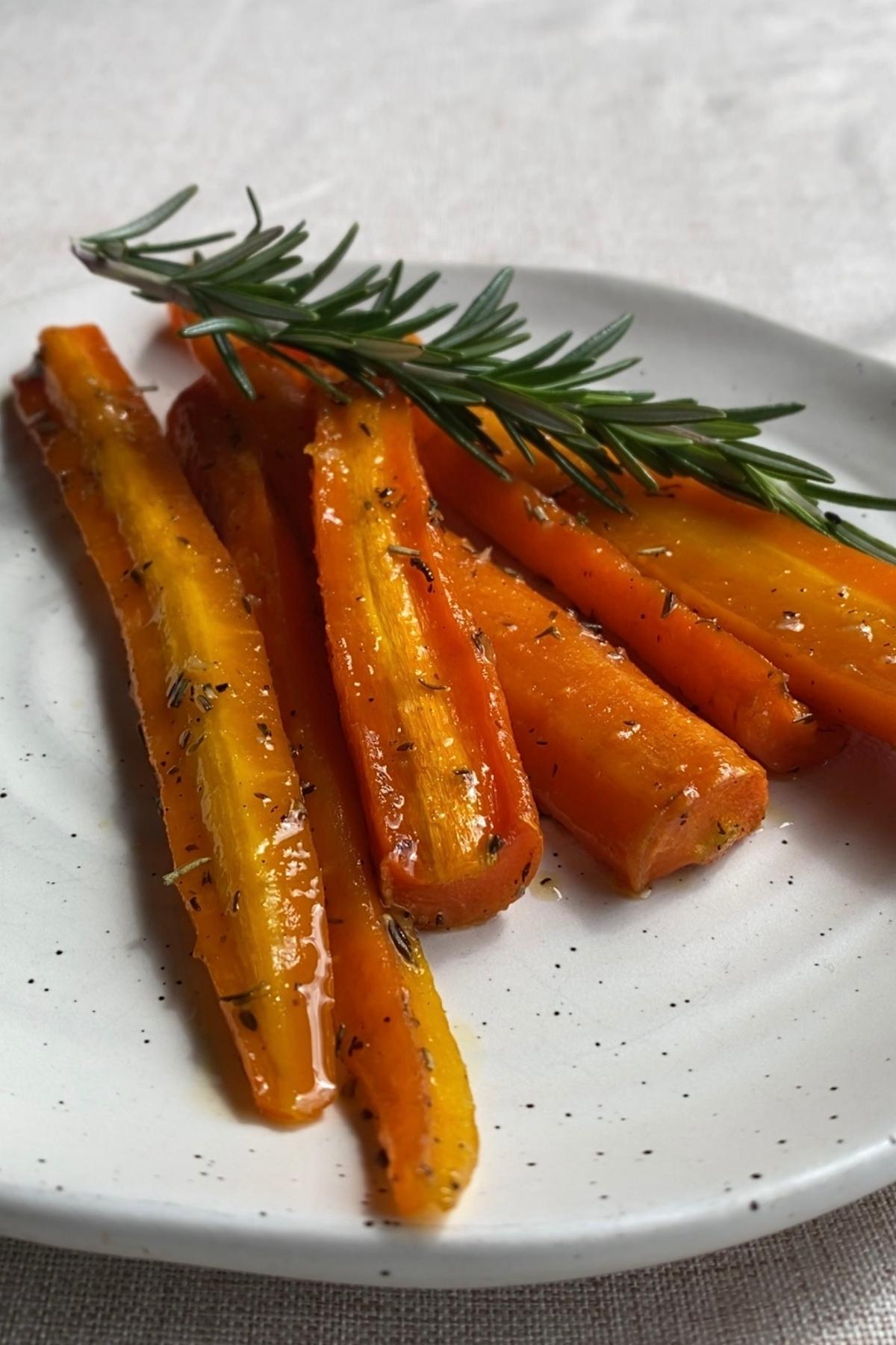 Plated roasted carrots with a shiny glaze and a fresh rosemary garnish.