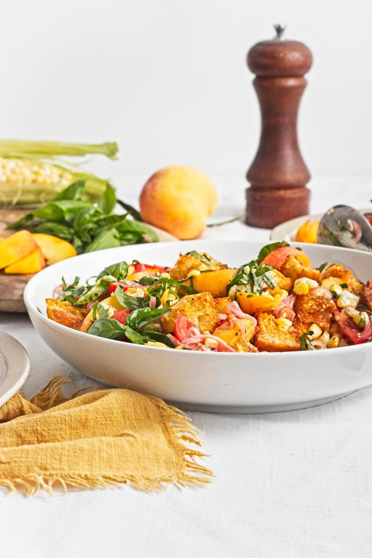 Side angle of peach and corn panzella salad showing roasted corn, tomatoes, peaches, and croutons.