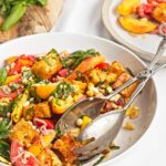 Side angle of peach and corn panzella salad showing roasted corn, tomatoes, peaches, and croutons.