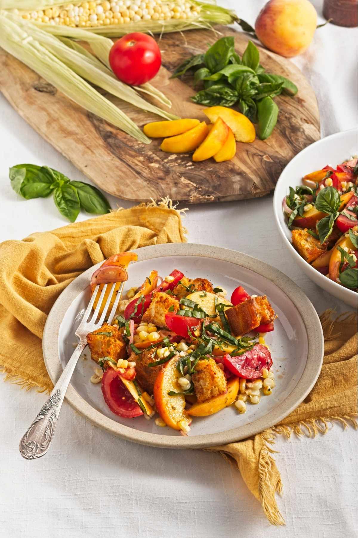 Close-up of peach and corn panzella salad with basil leaves, toasted croutons, and tangy dressing.