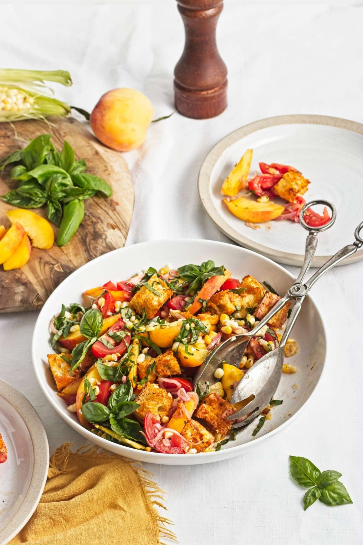 Close-up of peach and corn panzella salad with basil leaves, toasted croutons, and tangy dressing.