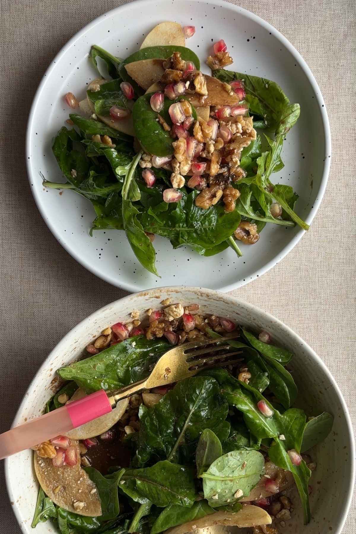 Close-up of pear salad with sliced pears, leafy greens, pomegranate arils, chopped nuts, and crumbled cheese in a ceramic bowl.