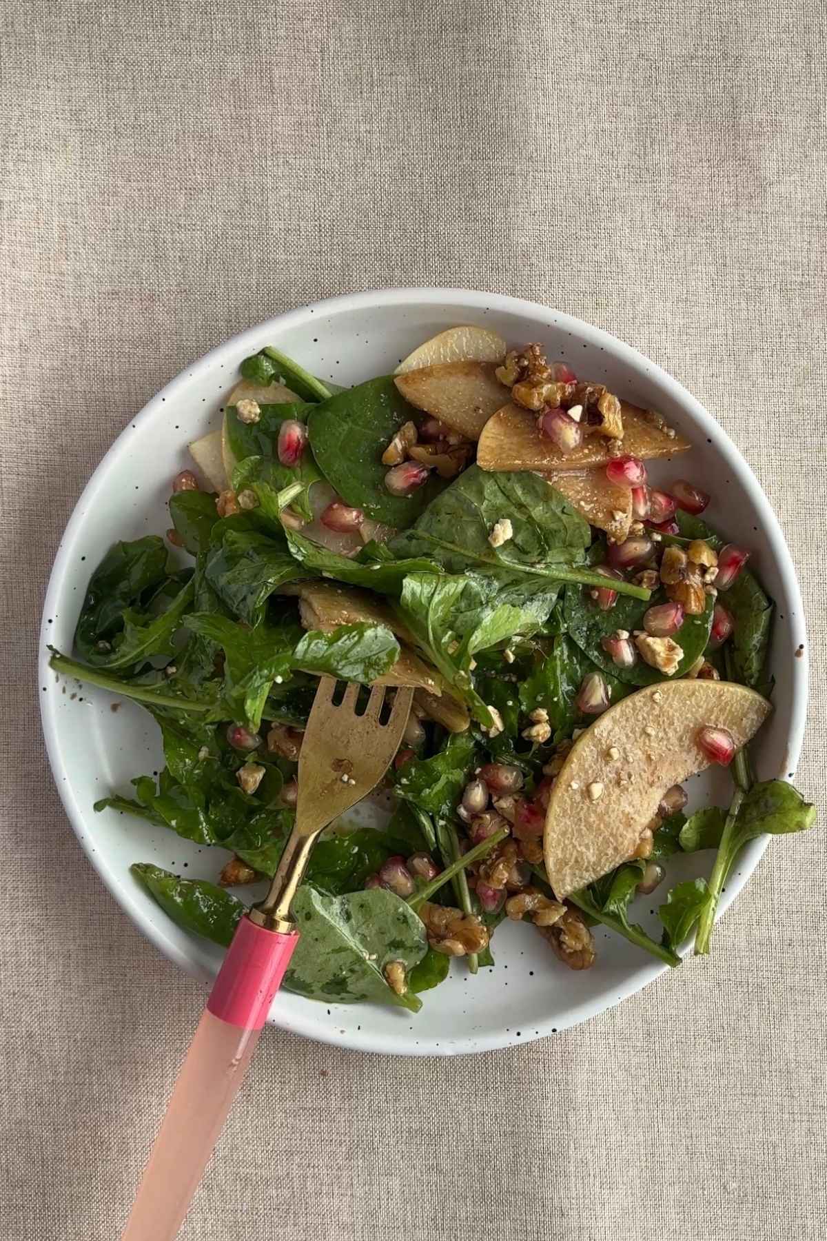 Two servings of pear salad shown from above, one plated and one in a mixing bowl, with spinach, pears, pomegranate, and nuts.