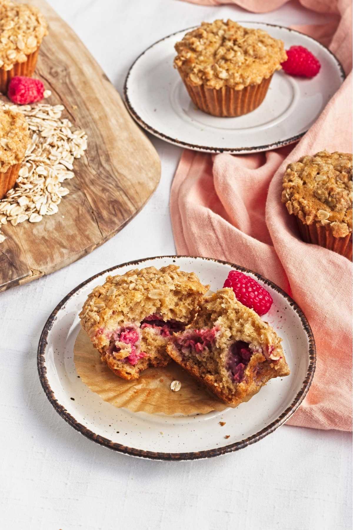 Vegan raspberry oat muffin cut in half to show the soft crumb and fresh raspberry pieces inside.