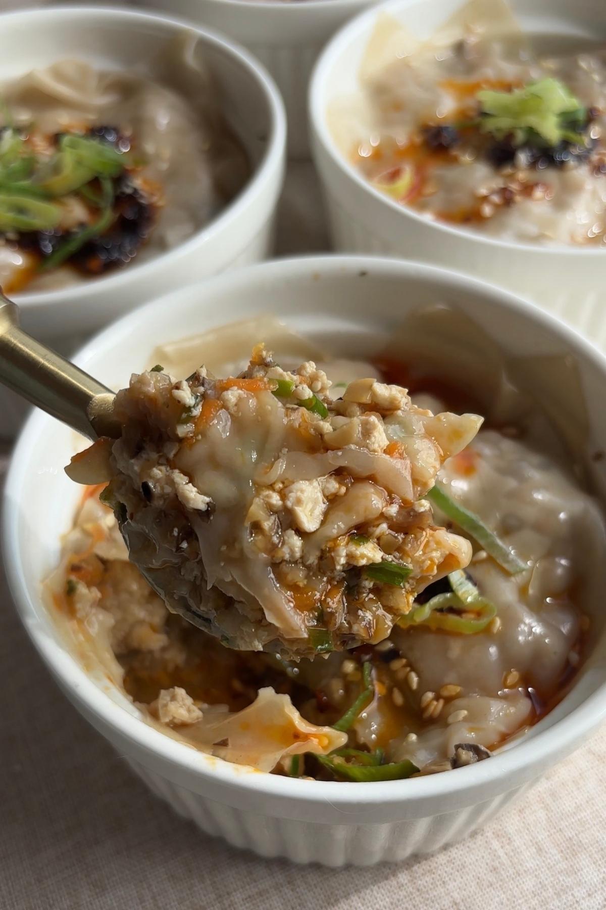 Spoon lifting layered wonton dumplings with tofu and mushroom filling from a ramekin.