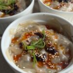 Steamed wonton dumpling bake in a ramekin topped with chili oil, sesame seeds, and scallions.