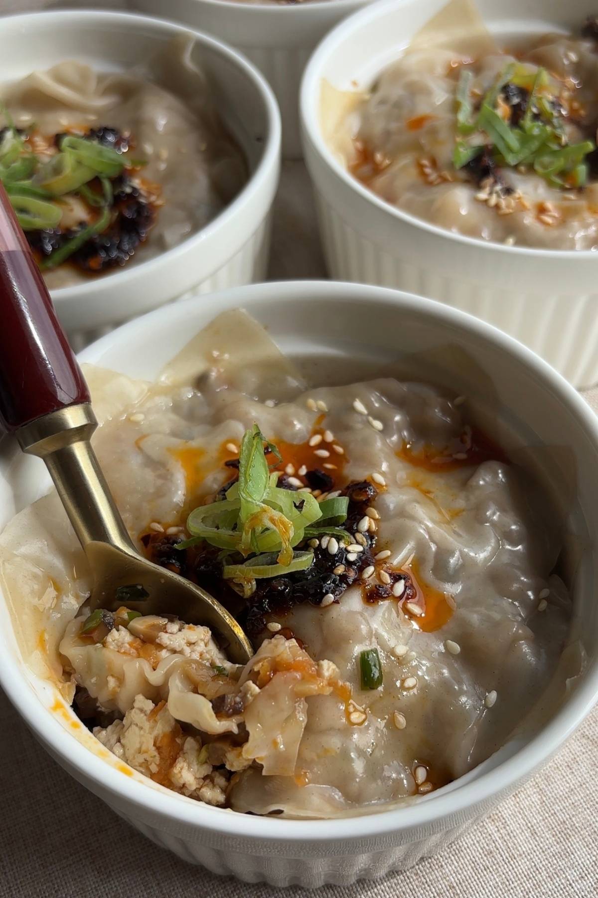 Several ramekins filled with steamed wonton dumplings, finished with chili oil and scallions.