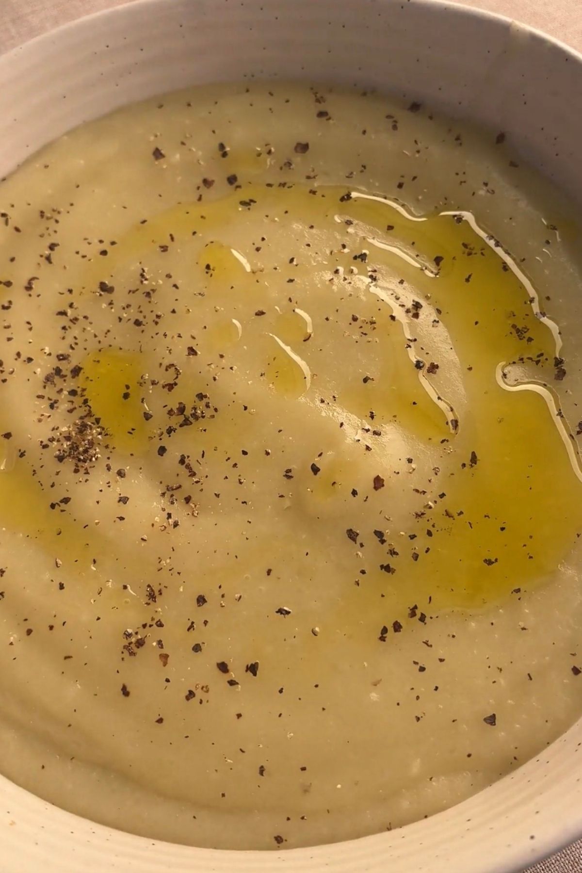 Close-up of blended potato soup with olive oil swirled on top and freshly cracked black pepper.