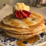 Stack of fluffy pancakes drizzled with syrup and topped with strawberries and a scoop of vanilla ice cream.