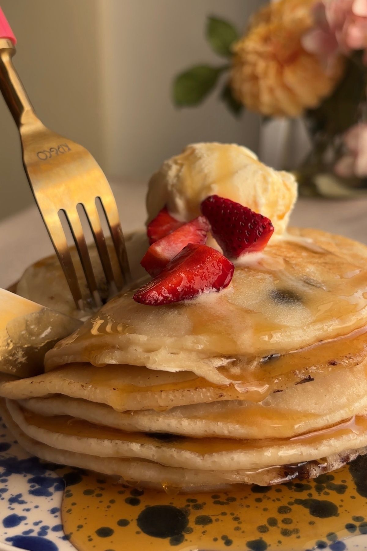 Fork cutting into a pancake stack with syrup, strawberries, and melting vanilla ice cream.