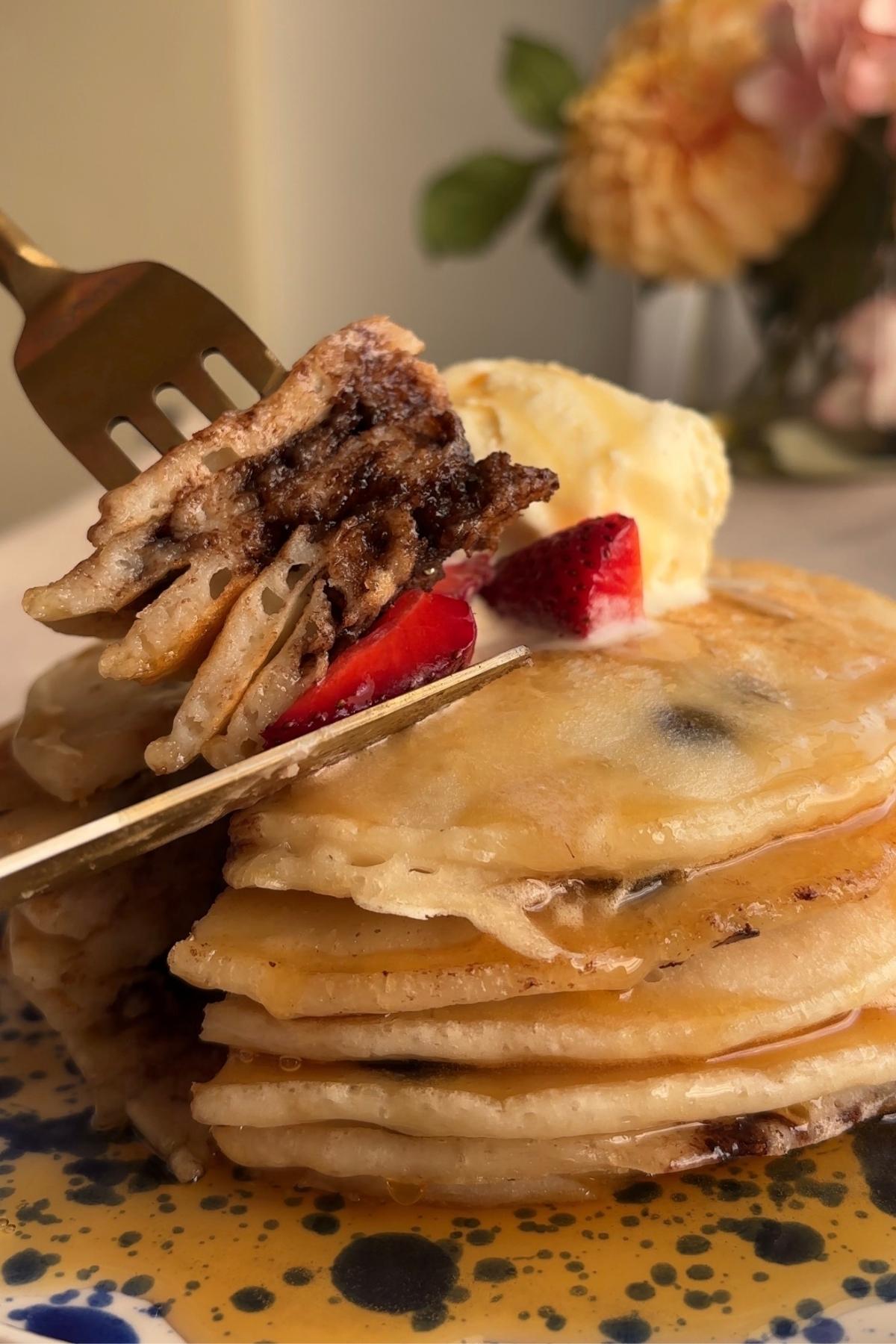 Fork lifting a bite of chocolate chip pancake with strawberry and syrup.
