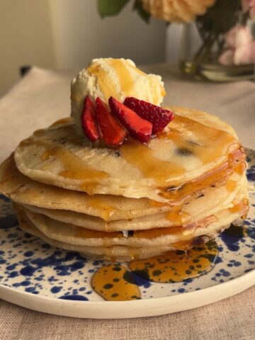 Stack of fluffy pancakes drizzled with syrup and topped with strawberries and a scoop of vanilla ice cream.