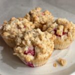 Vegan raspberry muffins with a golden oat streusel topping, served on a plate.