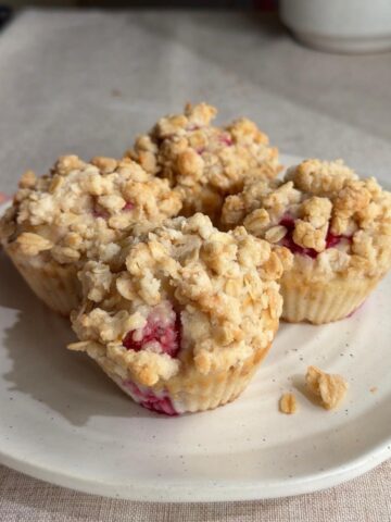 Vegan raspberry muffins with a golden oat streusel topping, served on a plate.
