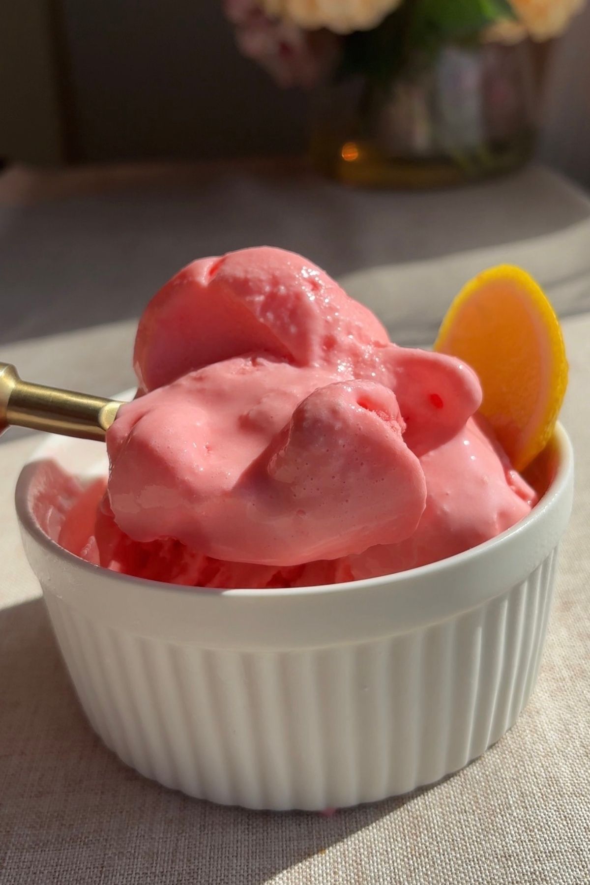 A spoon lifting soft pink sorbet from a ramekin, showing a glossy, creamy texture.