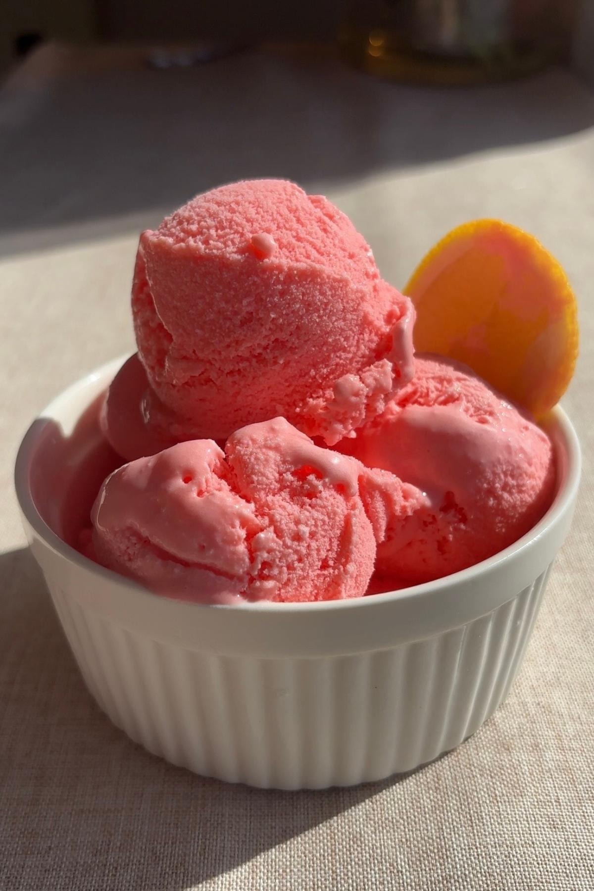 Scoops of pink sorbet in a white ramekin, garnished with a thin slice of lime.