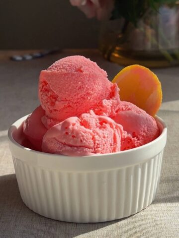 Three scoops of pink sorbet stacked in a white ramekin, with a smooth, slightly icy texture.