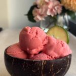 Four scoops of pink sorbet in a coconut bowl with a lime wedge.