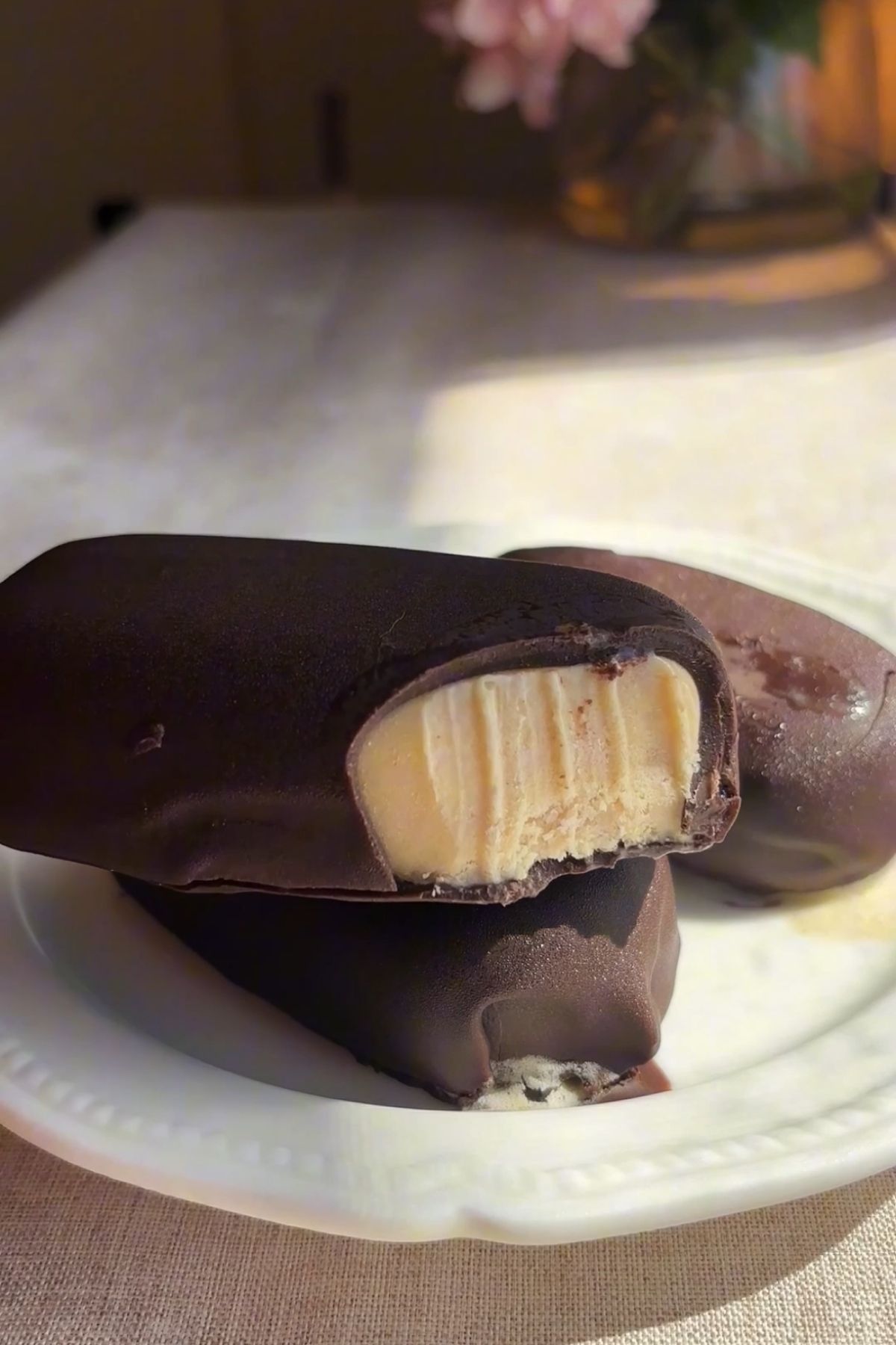 Vegan chocolate-covered ice cream bars on a white plate with wooden sticks