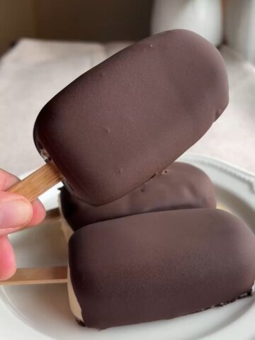 Hand holding a vegan chocolate-coated ice cream bar with smooth snap shell