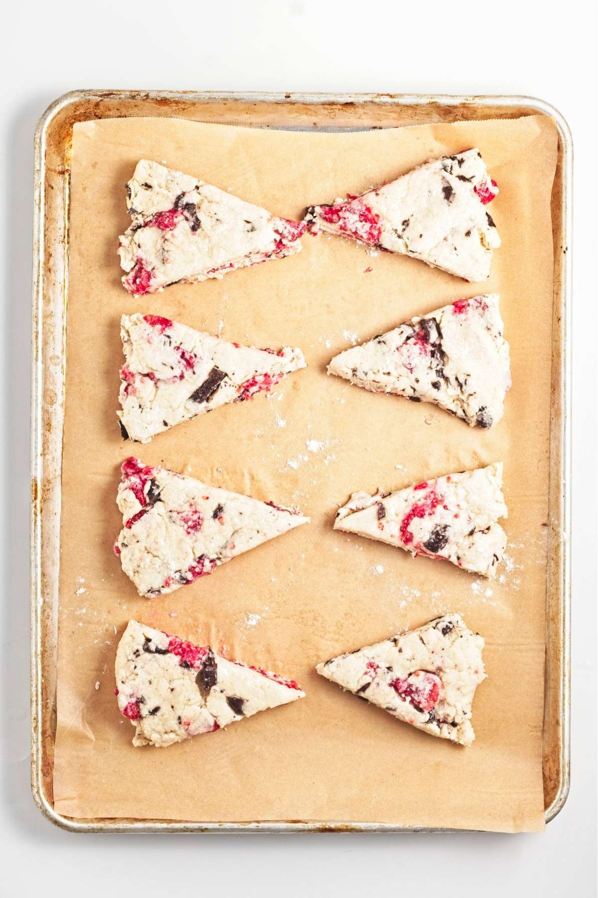 Unbaked scone wedges arranged on a parchment-lined baking sheet.