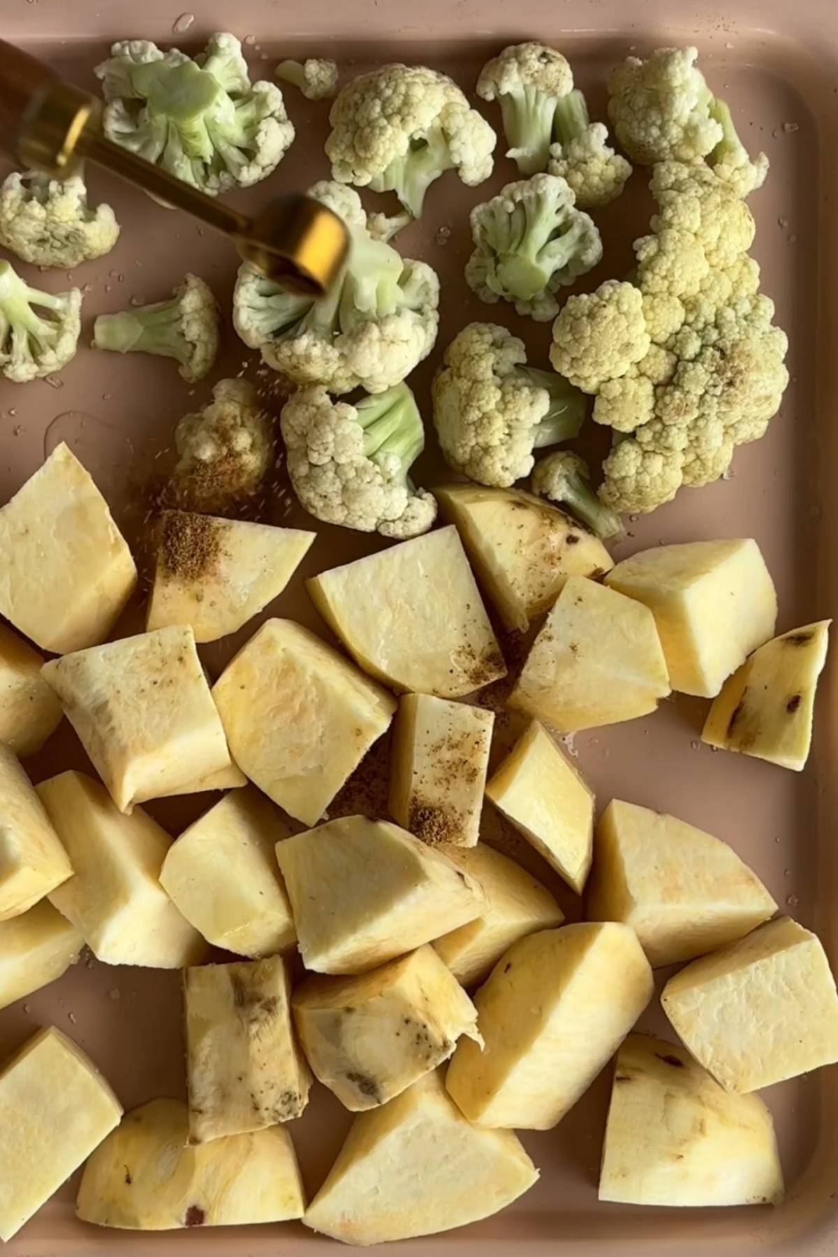 Cubed sweet potato and cauliflower florets on a tray, lightly seasoned before roasting.