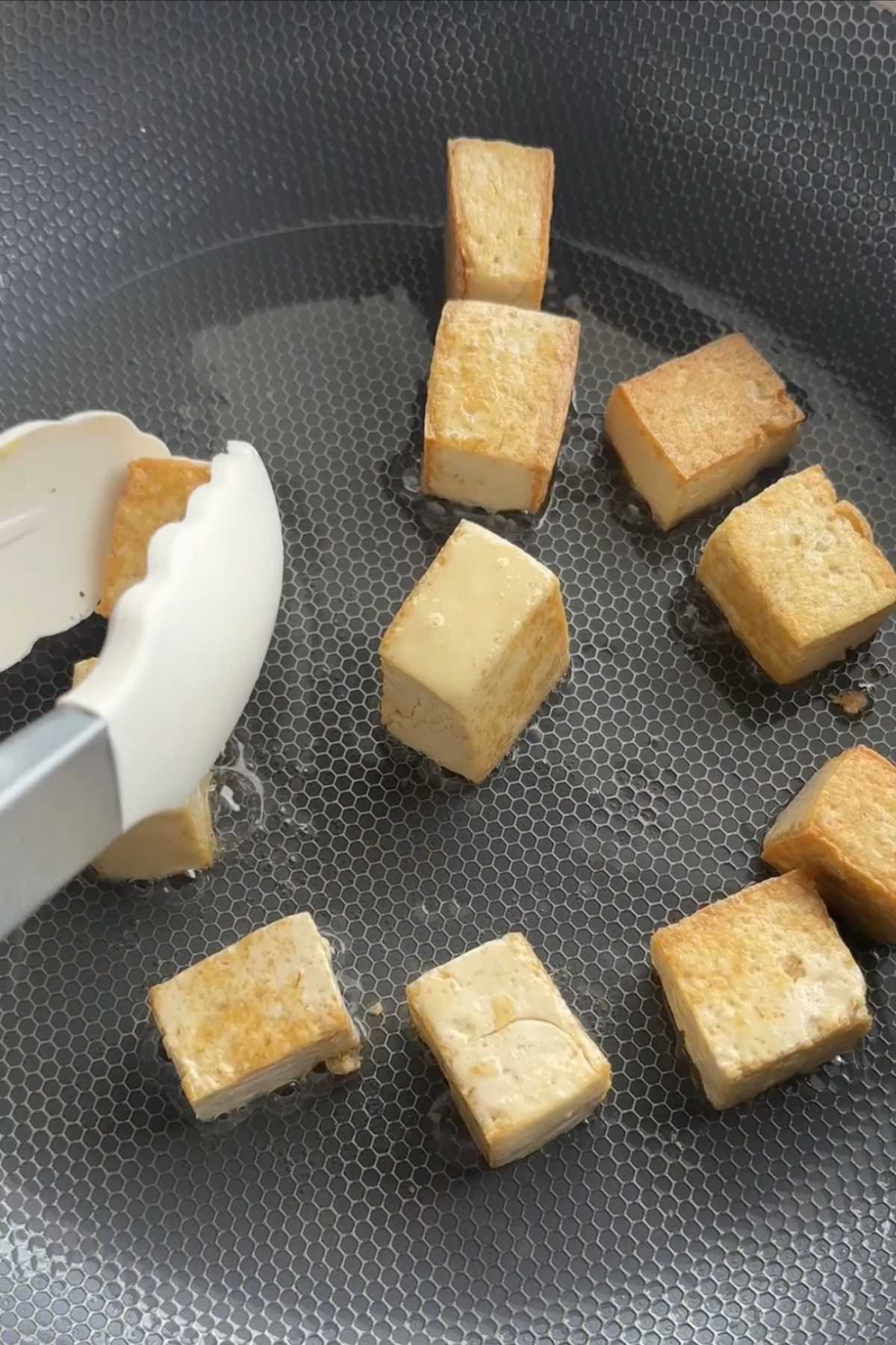Tofu cubes pan-frying until golden on all sides in a non-stick pan.