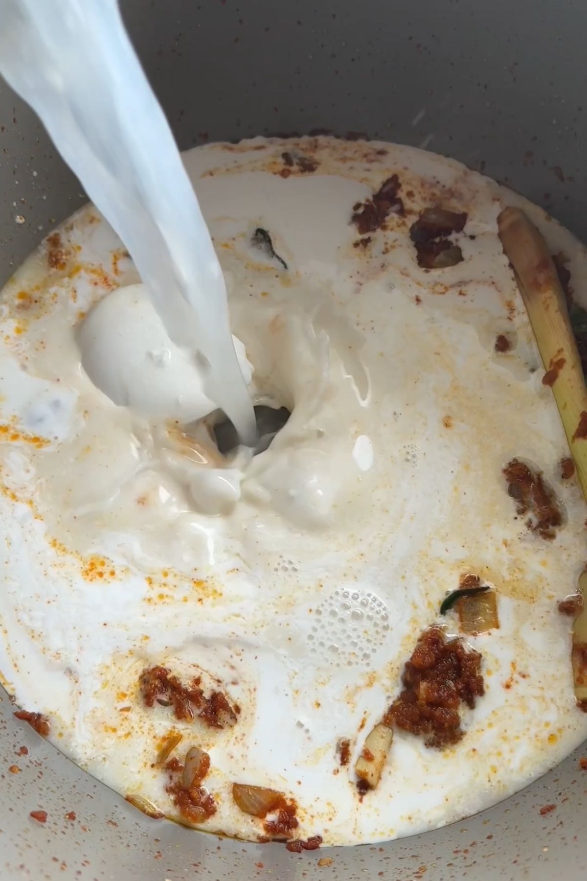 Coconut milk being poured into curry paste to form a creamy sauce.