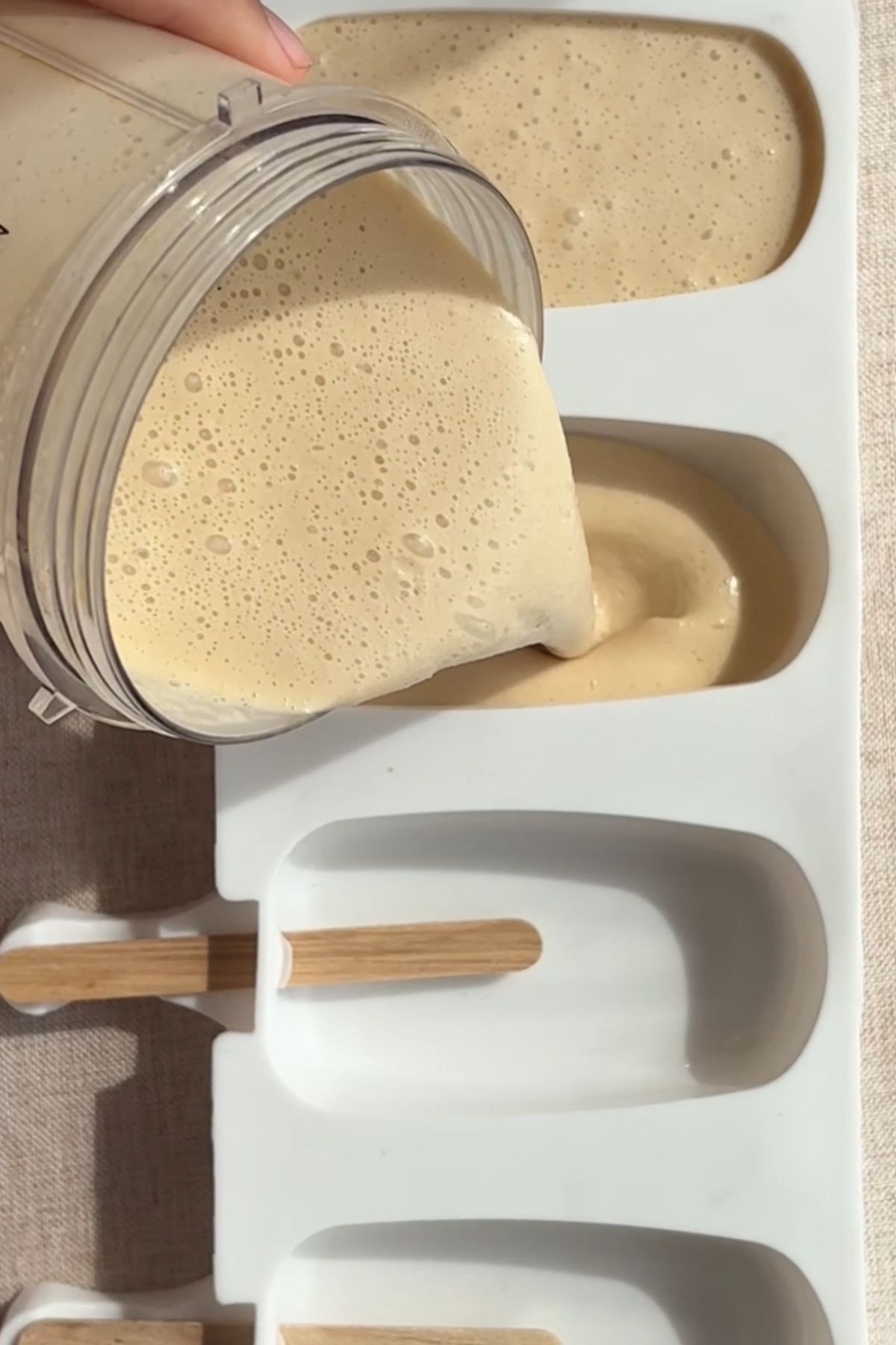 Creamy blended vegan ice cream mixture poured into silicone popsicle molds with wooden sticks