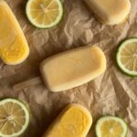 Several mango popsicles on brown paper with fresh lime slices placed between them.