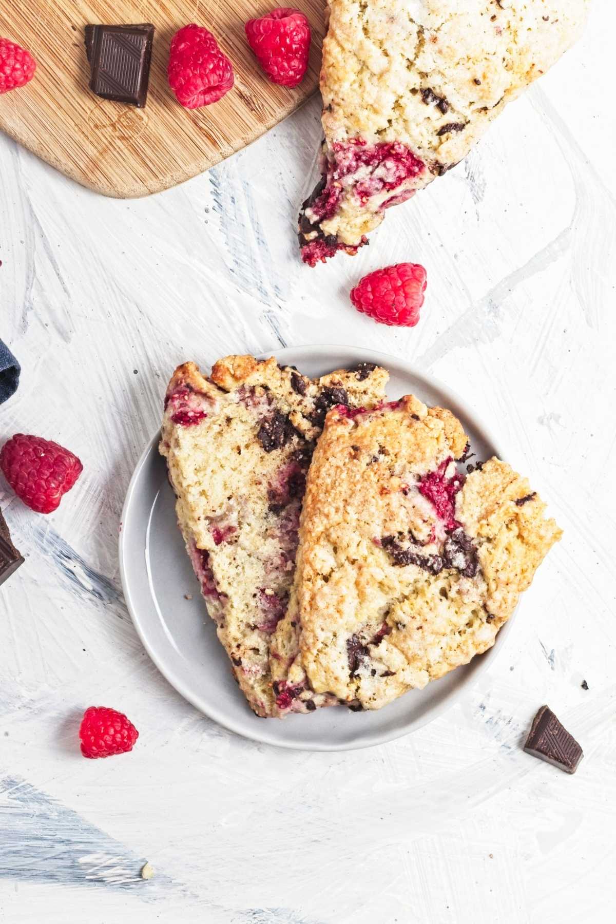 Two raspberry chocolate scones on a plate with scattered chocolate pieces.