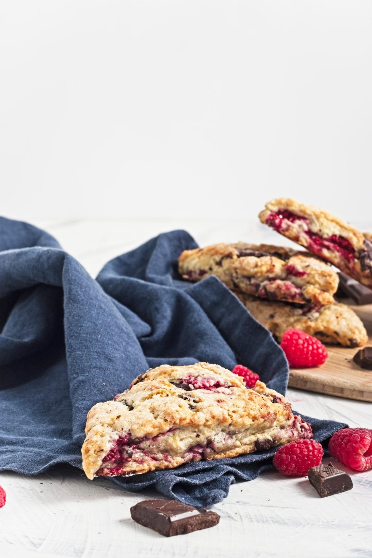 Golden scones with raspberries and dark chocolate on a wooden board with fresh berries.
