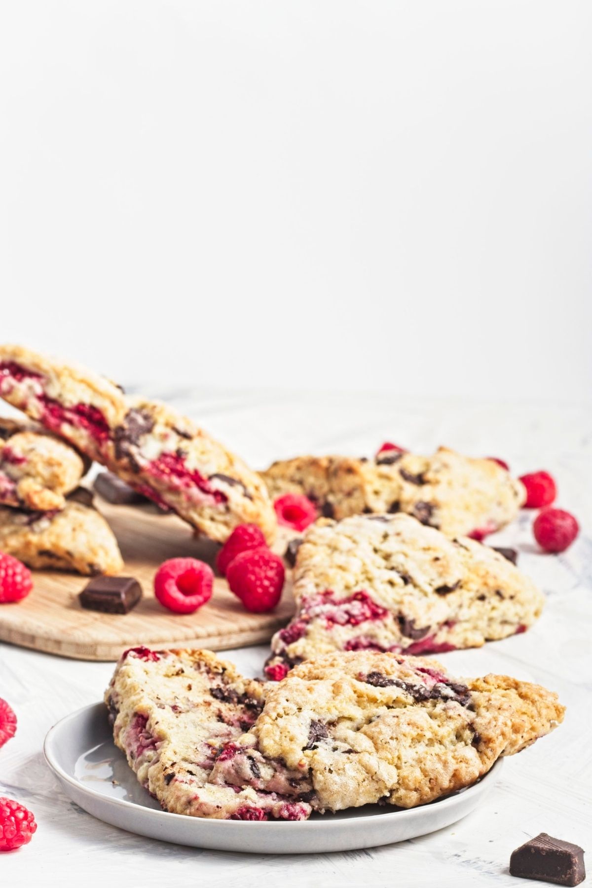 Stacked raspberry chocolate scones on a board with fresh raspberries.