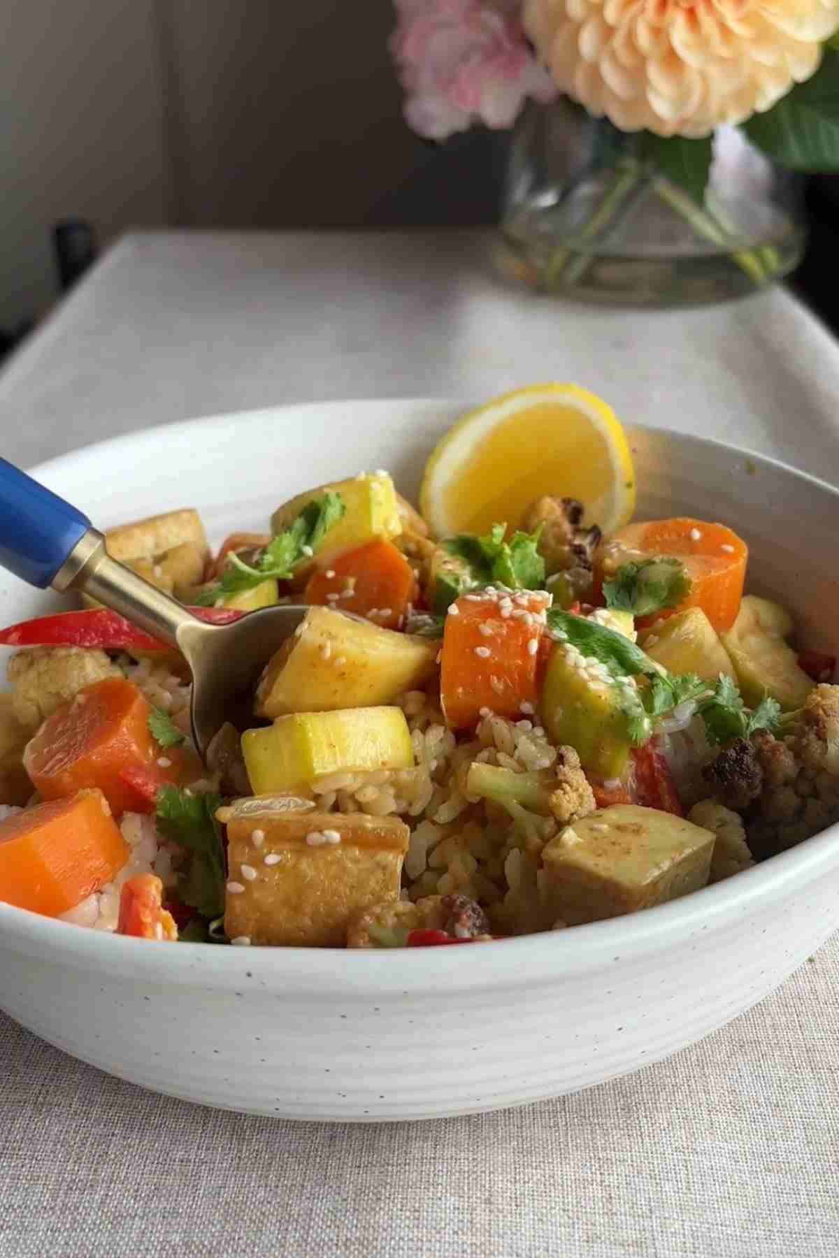 Bowl of vegan yellow curry with tofu, vegetables, and sesame seeds served over rice.