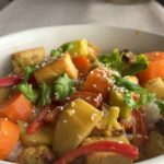Close-up of yellow curry with tofu cubes, sweet potato, cauliflower, and carrots on rice.